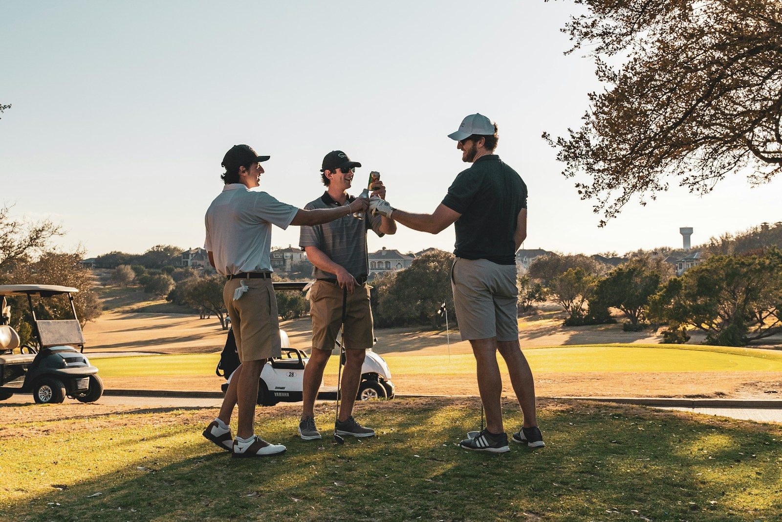 Three men in golf attire toasting with drinks on a sunny golf course